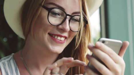 Hermosa-joven-charlando-en-el-teléfono-móvil-con-amigo.-Mujer-escriba-masaje-en-smartphone-en-café-y-sonriendo.