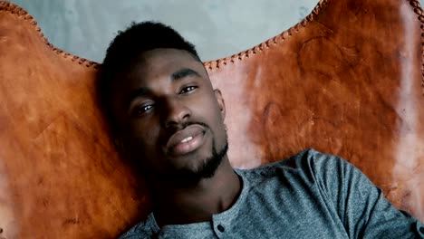 Handsome-African-man-with-the-beard-is-sitting-in-the-chair-and-smiling.-A-male-looks-dreamy,-thoughtful-and-calm