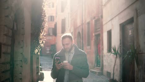 Lächelnde-junge-Mann-zu-Fuß-in-die-Stadt-am-Morgen-und-mit-Smartphone.-Guy-Surfen-im-Internet,-SMS-mit-jemandem