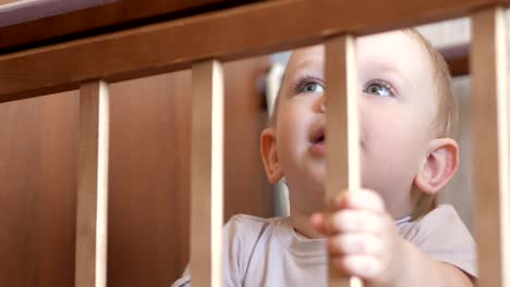 Cute-blond-babe-shows-playing-in-a-baby-crib-with-a-bolt.-He-smiles-and-twists-it-in-his-arms