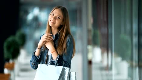 Mujer-joven-con-bolsas-sonriendo-y-posando.-Luces-de-tiendas-en-fondo