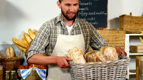 Portrait-of-male-staff-holding-breads-in-basket-at-bakery-section