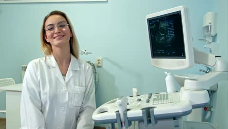 Smiling-female-doctor-in-glasses-looking-into-the-camera-in-ultrasound-room