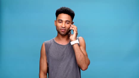 Young-smiling-african-man-talking-by-phone-over-blue-background.