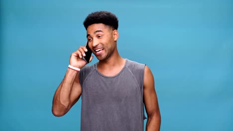 Young-smiling-african-man-talking-by-phone-over-blue-background.