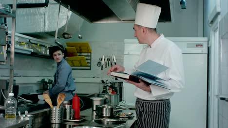 Head-chef-looking-for-recipe-in-a-book-while-checking-upon-his-cook-trainee
