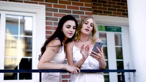 Girlfriends-look-at-photos-that-were-taken-during-the-holidays-on-the-smartphone,-the-ladies-stand-outside-in-a-warm-summer-day