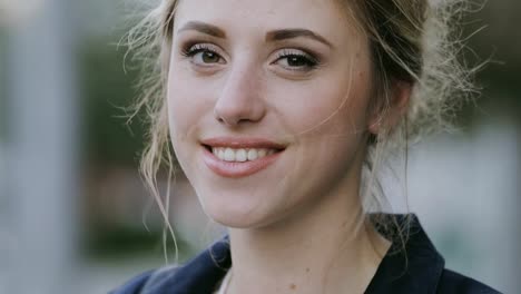 Closeup-face-of-cute-smiling-woman-looking-to-camera-in-city.-Wind-blows-her-hair.