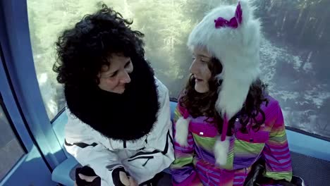 Young-woman-and-daughter-tourist-having-fun-in-cable-car-on-the-way-to-the-top-of-mountain-ski-slope