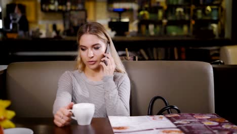 A-young-and-pretty-woman-holds-a-phone-in-her-hand-and-communicates-with-a-guy,-a-lady-came-into-a-cafe-to-have-a-cup-of-coffee