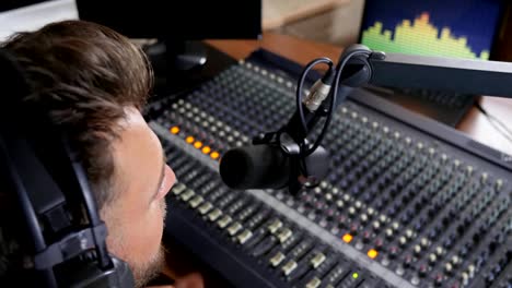 job-on-radio,-male-in-headphones-speaks-in-microphone-beside-audio-console