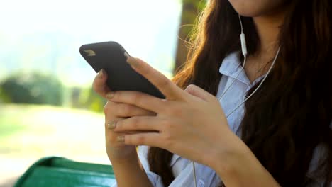 Cute-woman-is-reading-pleasant-text-message-on-mobile-phone-while-sitting-in-the-park-in-warm-spring-day,gorgeous-female-is-listening-to-music-in-headphones-and-searching-information-on-cell-telephone