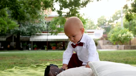 curious-child-in-bow-tie-plays-with-photo-camera-on-green-plaid-at-park