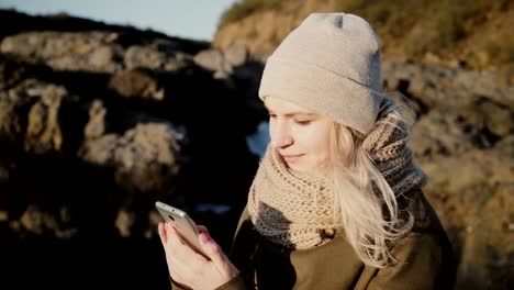 Young-blonde-woman-standing-in-mountains-place-and-taking-selfie-photo-on-smartphone-against-the-beautiful-background