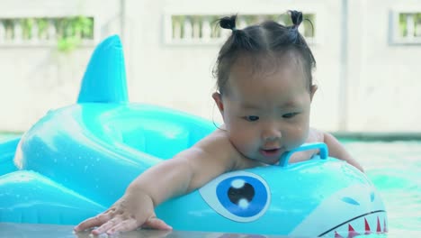 Niña-asiática-jugando-con-el-colorido-anillo-inflable-en-piscina