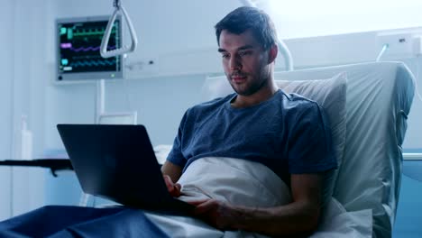 In-the-Hospital,-Recovering-Male-Patient-Uses-Laptop-while-Lying-on-the-Bed.-Working-even-when-Sick-and-in-Hospital.-Nurse-Checks-Drop-Counter.