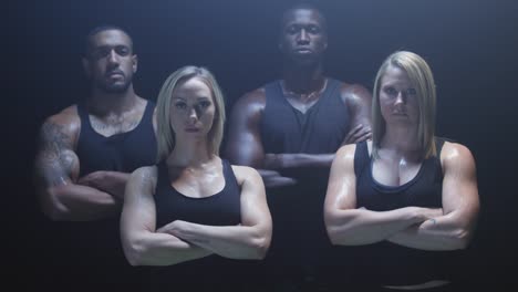 Group-of-athletes-staring-at-the-camera-crossing-their-arms-on-a-foggy-dark-background