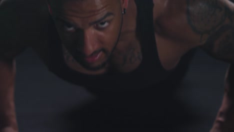 Muscular-black-man-doing-some-push-ups,-and-maintaining-his-position-on-a-dark-background
