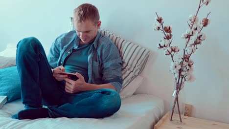 Young-man-looking-at-the-phone-screen,-relaxing-on-the-couch-in-the-room