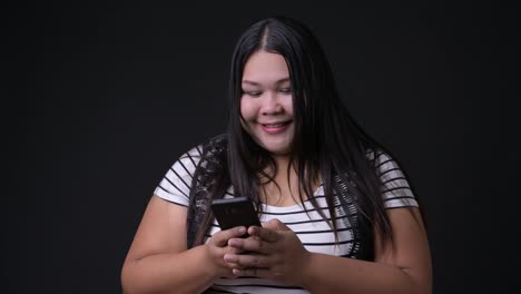 Beautiful-overweight-Asian-woman-using-mobile-phone-against-black-background