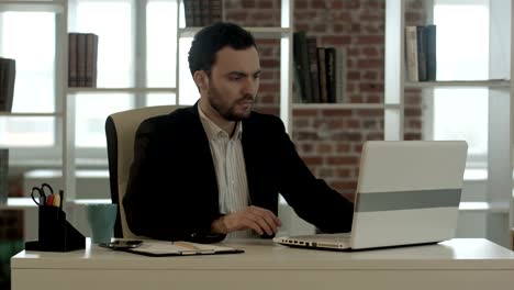 Young-stressed-businessman-working-on-computer-laptop-late-at-night-in-suit-and-tie-isolated-on-black-background-looking-frustrated-watching-on-internet-disaster-work-situation