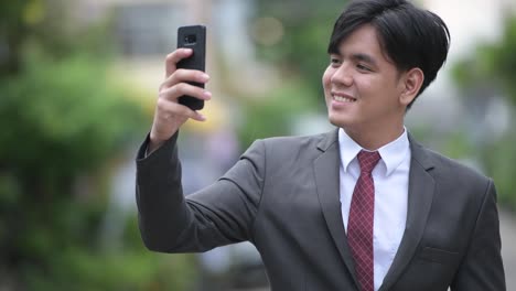 Young-handsome-Asian-businessman-using-phone-in-the-streets-outdoors