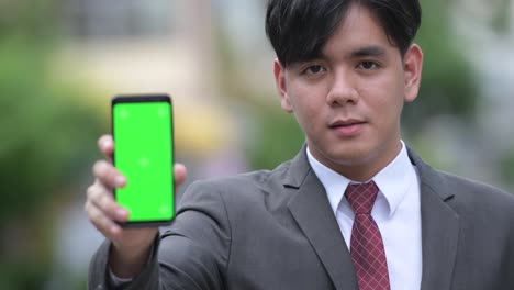 Young-handsome-Asian-businessman-showing-phone-in-the-streets-outdoors