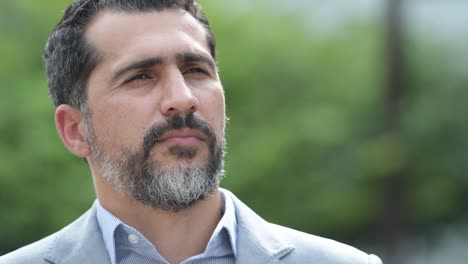 Handsome-Persian-bearded-businessman-smiling-while-thinking-in-the-streets-outdoors