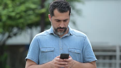 Handsome-Persian-bearded-man-using-phone-in-the-streets-outdoors