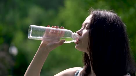 Close-up-of-a-happy-looking-asian-woman-drinks-water-from-a-transparent-bottle.-Sunrays-are-on-her-face.