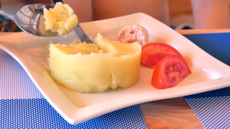 Una-cuchara-de-mujer-reúne-a-puré-de-patatas-con-tomates-y-alimenta-al-bebé.