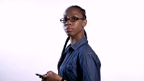 Young-beautiful-african-american-woman-in-glasses-texting-on-phone-and-looking-at-camera,-profile-of-black-model-in-studio-with-phone,-serious