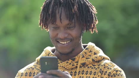 Young-happy-handsome-African-man-smiling-while-using-phone-in-the-streets-outdoors