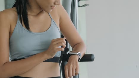 Retrato-de-joven-asiática-está-buscando-en-sus-relojes-inteligentes-en-el-gimnasio