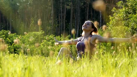 Joyful-Woman-Sitting-on-the-Green-Lawn-Happily-Lifts-her-Hands-Up-to-the-Sky-on-Scenic-Field-at-Sunset-Background