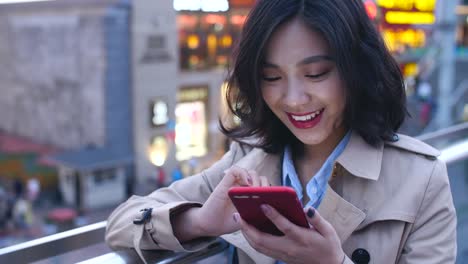 Una-muy-feliz-asiático-joven-utilizando-el-teléfono-móvil-en-la-ciudad-en-la-noche