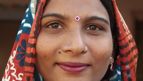 Extreme-close-up-of-a-gorgeous-Indian-woman's-face-smiling-laughing-happy-joy-jovial-looking-at-camera-in-traditional-dress-head-covered-bindi-pretty-jewelry-at-home-freedom-love-static-shot-lock-down