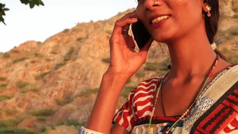 Handheld-shot-of-young-woman-talks-calls-mobile-phone-communication-device-connectivity-signal-wireless-smiles-happy-at-sunset-on-a-hill-outdoor-nature-hot-summer-day-magic-hour-beautiful-serene-love