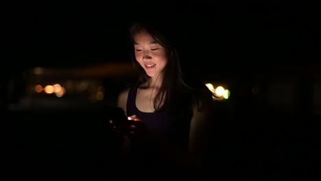 Beautiful-Asian-Woman-Outdoors-At-Night-Using-Mobile-Phone