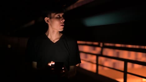 Portrait-Of-Asian-Man-Outdoors-At-Night-In-Parking-Lot-Using-Mobile-Phone