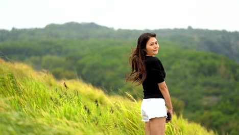 Asian-female-tourists-stand-happily-on-the-scenic-spot.-The-background-is-a-mountain-view-and-a-beautiful-pasture.