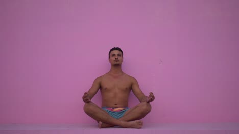 Mixed-race-hispanic-young-man-with-naked-torso-practicing-yoga-fitness-exercise-on-pink-background.-Sport,-meditation-and-lifestyle-concept.-Peaceful-Meditation-for-good-health