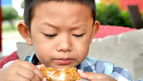 Cute-asian-boy-are-happy-eating-fried-chicken-leg-in-restaurant.-Video-4k-Slow-motion