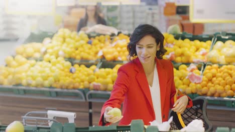 Im-Supermarkt:-Portrait-of-Beautiful-Smiling-Frau-Wahl-Bio-Früchte-In-frischen-Produkten-Gang-und-setzt-sie-in-Warenkorb.-High-Angle-Shot.