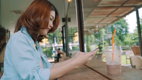 Fröhlich,-glücklich-junge-Asiatin-sitzen-trinken-Eistee-grüner-Tee-im-Café-mit-Smartphone-zum-sprechen,-lesen-und-SMS.-Frauen-Lifestyle-Konzept.