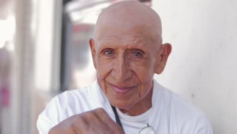 An-old-bald-hispanic-man-smiles-at-the-camera-on-the-street-of-Mexico