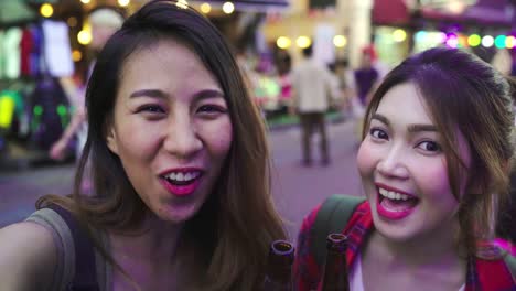 Reisender-Backpacker-Blogger-asiatische-Frauen-Lesben-LGBT-paar-Reisen-mit-Smartphone-für-Selfie-in-Thailand.-Weiblich,-trinken-Alkohol-oder-Bier-an-der-Khao-San-Road-die-berühmteste-Straße-in-Bangkok.
