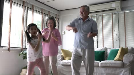 Pareja-senior-y-niños-chica-bailando-juntos-en-la-sala-de-estar-en-casa.-Concepto-de-familia-feliz,-excitar-partido,-salud-mental-y-psicología-positiva.-resolución-de-4-k.