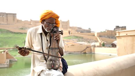 Eine-ältere-männliche-Straßenmusiker-klassische-indische-Musik-Musizieren-neben-See-in-Rajasthan