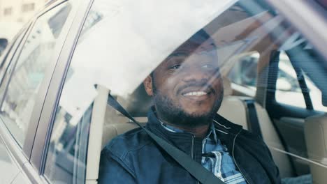 Handsome-Young-Black-Man-Rides-on-a-Passenger-Seat-of-a-Car,-Looks-in-Wonder-out-of-the-Window.-Big-City-View-Reflected-in-Window.-Camera-Mounted-outside-Moving-Car.